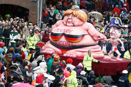 狂欢节上,德国总理默克尔与法国总统奥朗德身材对比鲜明,默克尔身上写着“德国经济”。(Getty Images) 狂欢节上,德国总理默克尔与法国总统奥朗德身材对比鲜明,默克尔身上写着“德国经济”。(Getty Images)