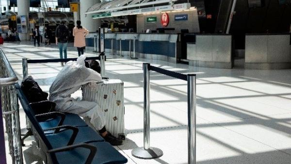 5月13日,一名身穿保护衣的男子在美国肯尼迪机场趴在行李箱上睡觉。(图片来源:JOHANNES EISELE/AFP via Getty Images)