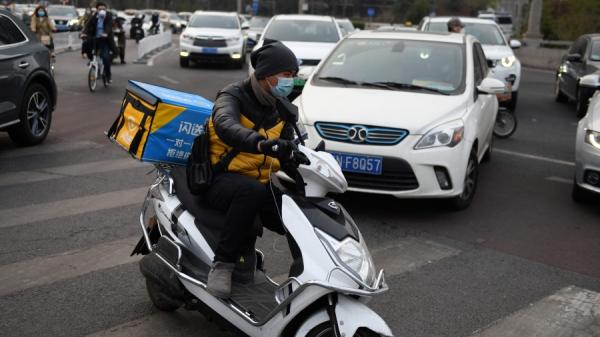 图为2020年3月24日,一名外送员在北京的一个十字路口驶过。(图片来源:GREG BAKER/AFP via Getty Images)