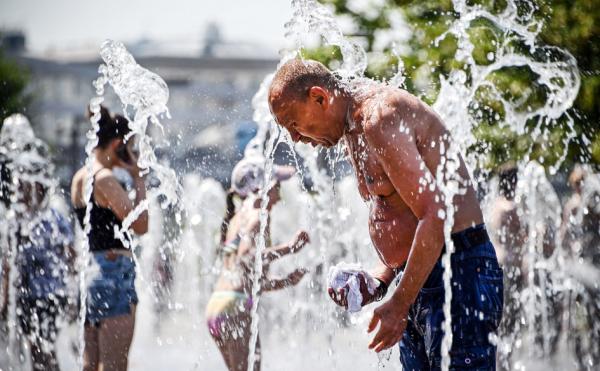 在极端高温天气下,一名男子在喷水池喷水降温。(ALEXANDER NEMENOV/AFP/Getty Images)