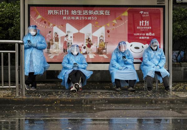 2022年11月11日,几位穿防护服的工作人员在北京一处购物节广告牌前。(Kevin Frayer/Getty Images)