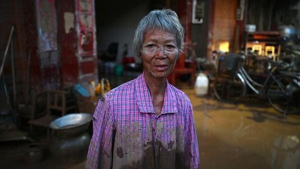 2026年7月9日,广西甘塘一名妇女站在自家房屋外,房屋被附近水库溃坝引发的洪水淹没。(图片来源:GREG BAKER AFP via Getty Images)