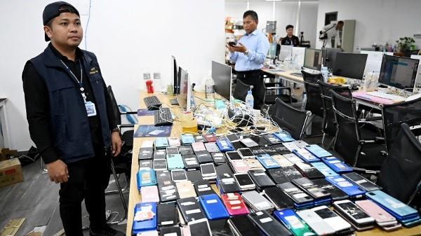 2026年3月11日,柬埔寨金边警方在前一晚突袭行动后,一名警员在一处网络诈骗指挥中心旁站岗,身边摆放着智能手机及其他查获的设备。(图片来源:TANG CHHIN Sothy/AFP via Getty Images)